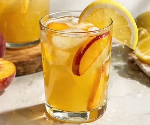 Fresh peach lemonade in a glass with a slice of peach and lemon garnish
