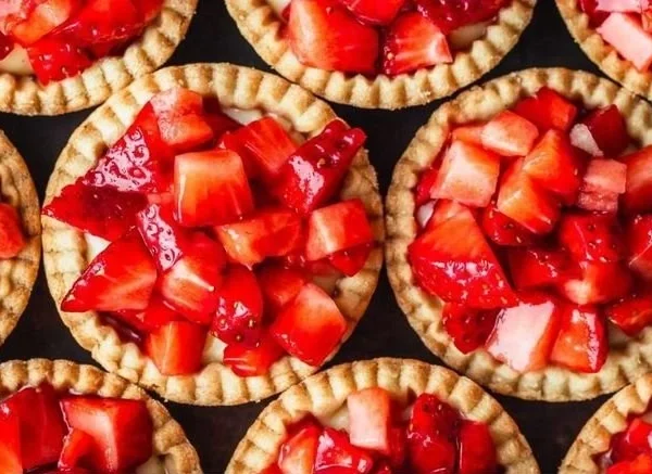 Mini strawberry tartlets topped with fresh strawberries and whipped cream.