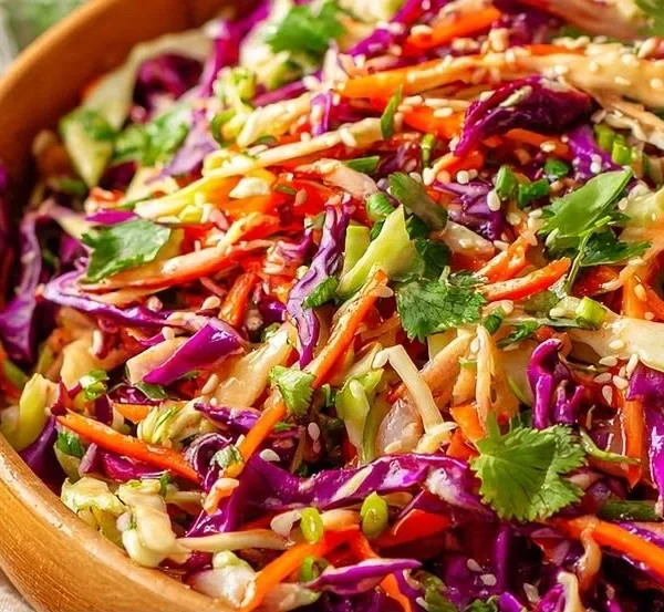 Bowl of simple Asian coleslaw topped with sesame dressing and colorful vegetables.