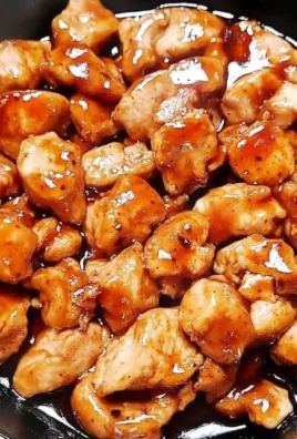 A plate of tasty teriyaki chicken bites garnished with sesame seeds and green onions.