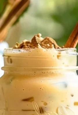 Creamy iced vanilla chai latte in a glass with spices and vanilla beans.