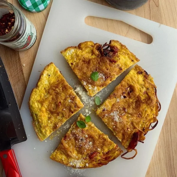 Delicious leftover pasta frittata garnished with herbs on a white plate.