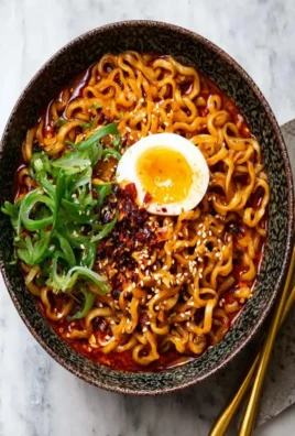 Bowl of spicy chili oil dry ramen garnished with green onions and sesame seeds.